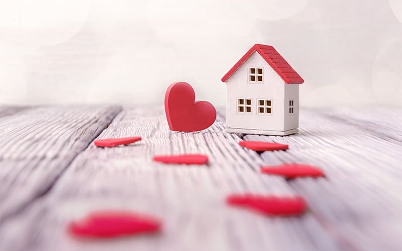 Toy house and red hearts on light defocused background